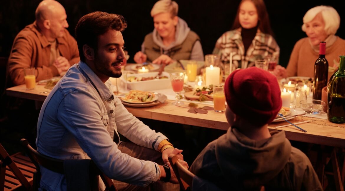 família sentada a mesa, com banquete farto servido, todos estão felizes e conversando