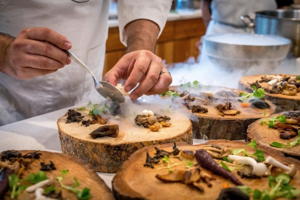 Chef finalizando prato, esse de madeira rústica, esta sendo servido cogumelos, batatas, aspargos e mais legumes usando a nano tecnologia de fumaça de gelo seco. A consultoria vegana auxilia na elaboração e harmonização dos sabores unindo com nutrientes.